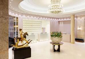 A luxurious lobby with marble walls, a reception desk, a chandelier, and a statue of a golden figure on a horse.