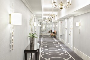 A hallway with a patterned carpet, wall sconces, and a chandelier.