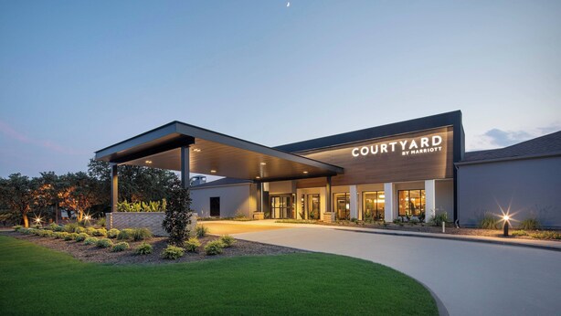 A Courtyard by Marriott hotel entrance with a covered walkway, landscaped garden, and a clear sky. - Courtyard by Marriott Addison Midway (Addison)