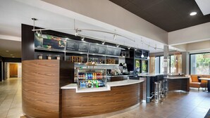 A modern bar area with a curved counter, beverage dispensers, and a menu board. - Courtyard by Marriott Addison Midway (Addison)