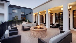 An outdoor patio area with a stone fire pit surrounded by wicker furniture and a seating area with cushions. - Courtyard by Marriott Addison Midway (Addison)