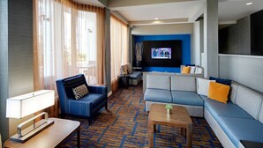 A modern hotel room with a sectional sofa, a blue armchair, a small table, and a TV mounted on the wall. - Courtyard by Marriott Addison Midway (Addison)