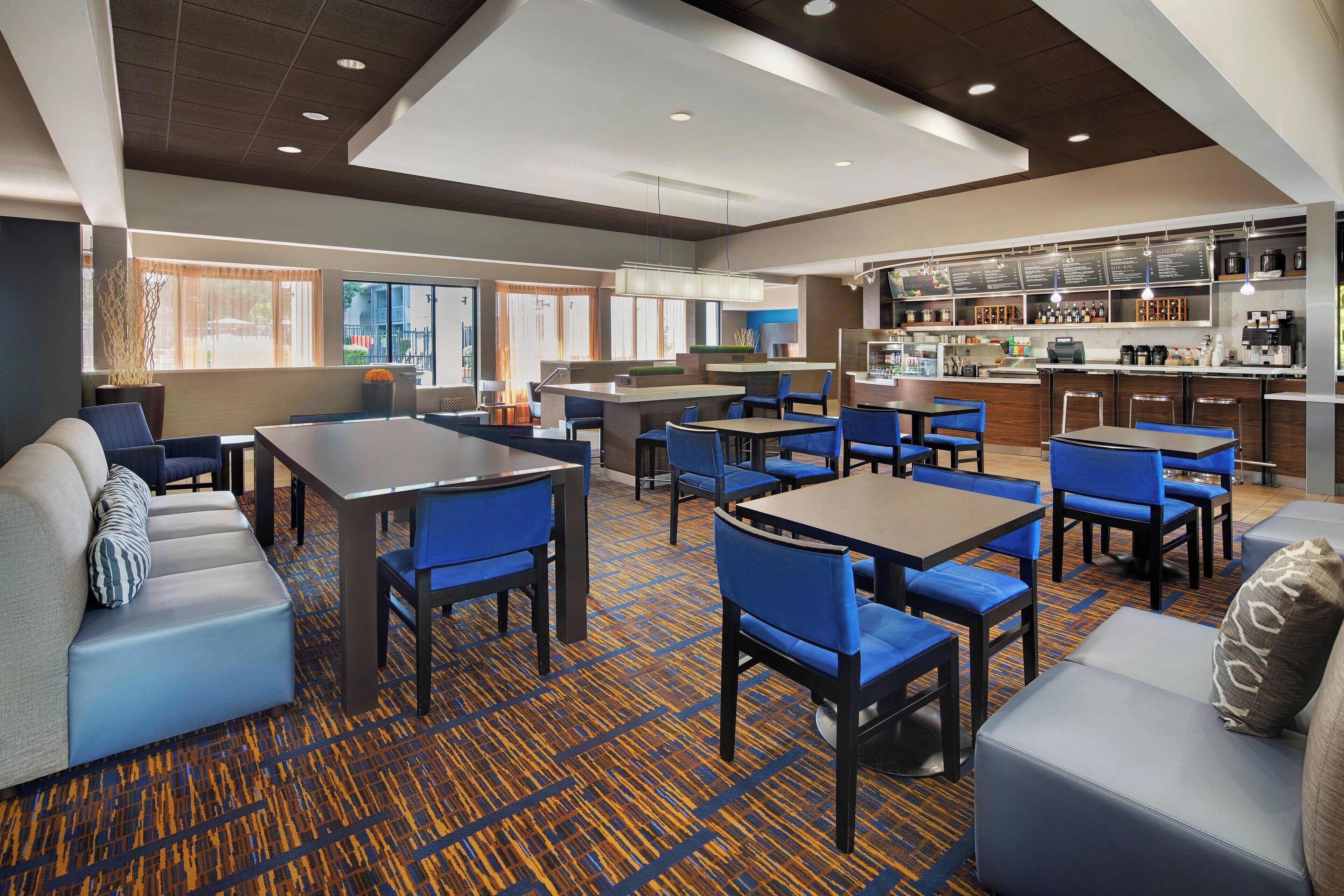 A hotel lobby with seating areas, a bar, and a kitchen in the background.