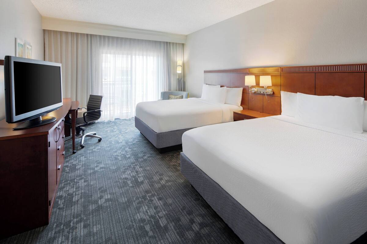 A hotel room with two beds, a TV, a desk, and a chair.
