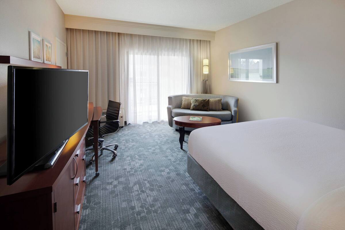A hotel room with a large bed, a television, a desk with a chair, a sofa, and a small table.