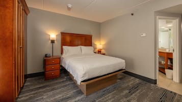 A bedroom with a bed, bedside lamps, a wooden nightstand, a wardrobe, and a bathroom visible through an open door.