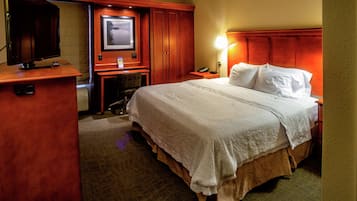Quarto de hotel com uma cama grande, uma mesa com computador, televisão e TV fixada na parede.