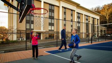 An outdoor basketball court with a chain-link fence, a basketball hoop, and a building in the background.