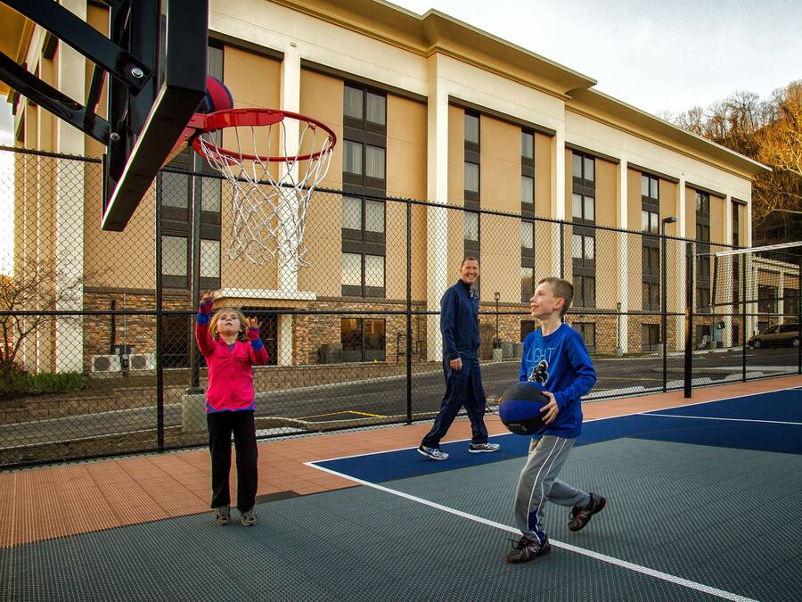 An outdoor basketball court with a chain-link fence, a basketball hoop, and a building in the background.