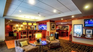 A lobby with two armchairs, a round table, a bar area, and a television screen. - Hampton Inn Wheeling (Wheeling)