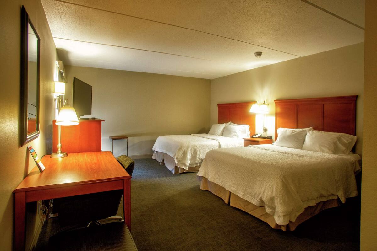 Habitación de hotel con dos camas, un escritorio y un espejo.