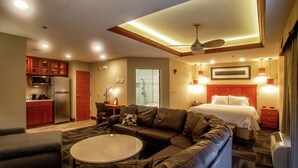 A modern hotel room with a kitchenette, a living area with a sofa and coffee table, a bed with a headboard, and a ceiling fan. - Hampton Inn Wheeling (Wheeling)