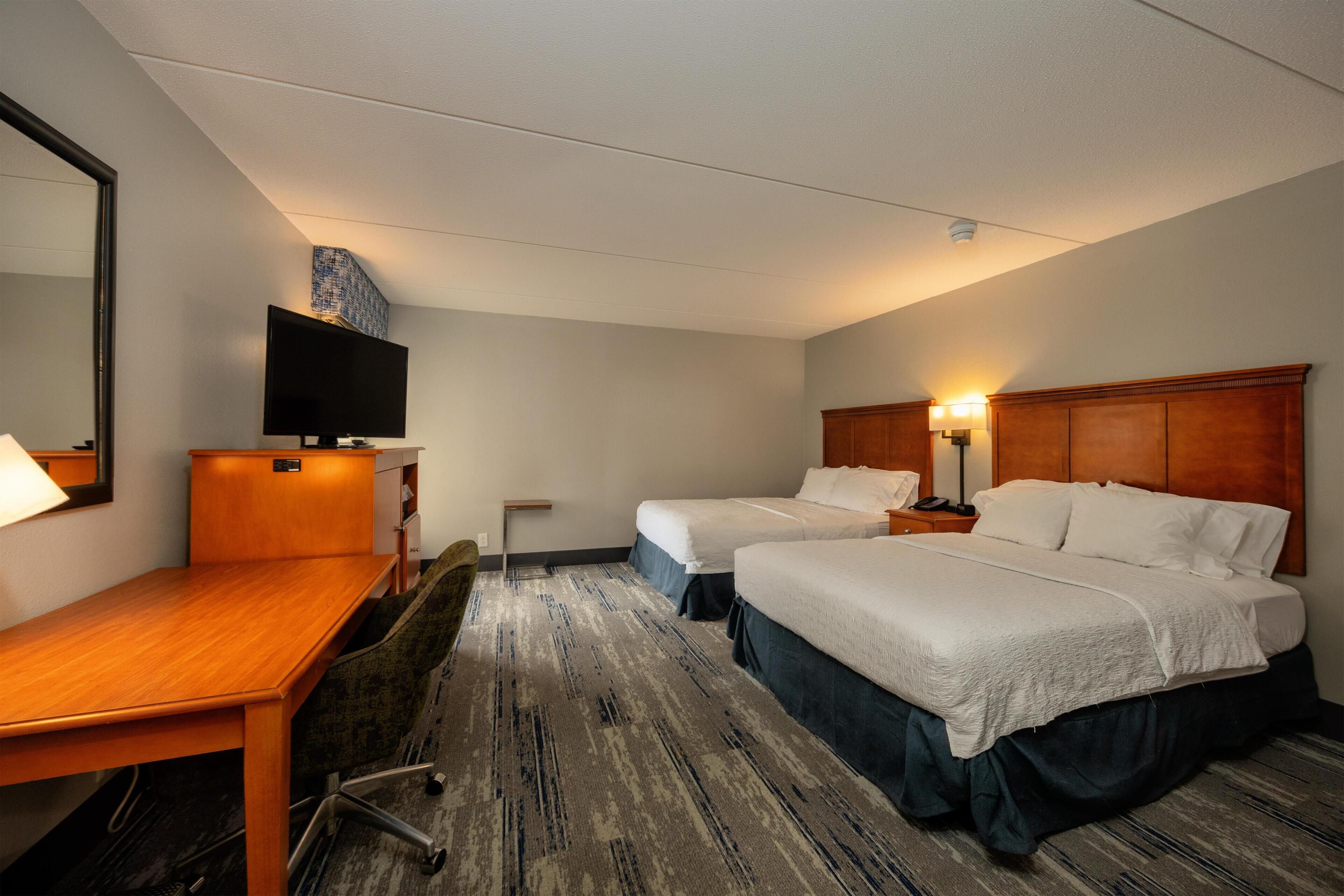 A hotel room with two beds, a desk, a chair, a television, and a mirror.