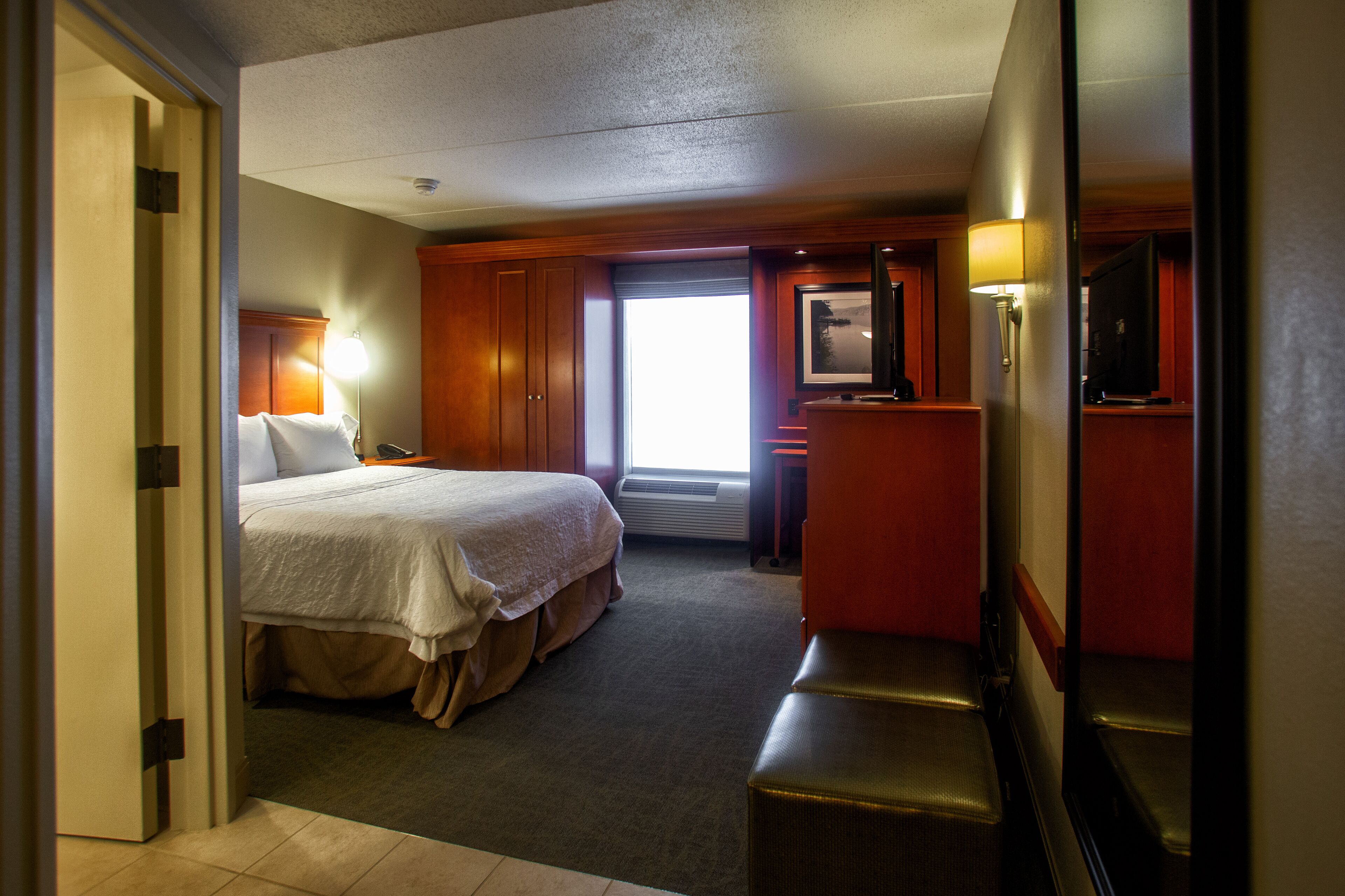 A hotel room with a bed, a desk, a chair, a TV, and a window.