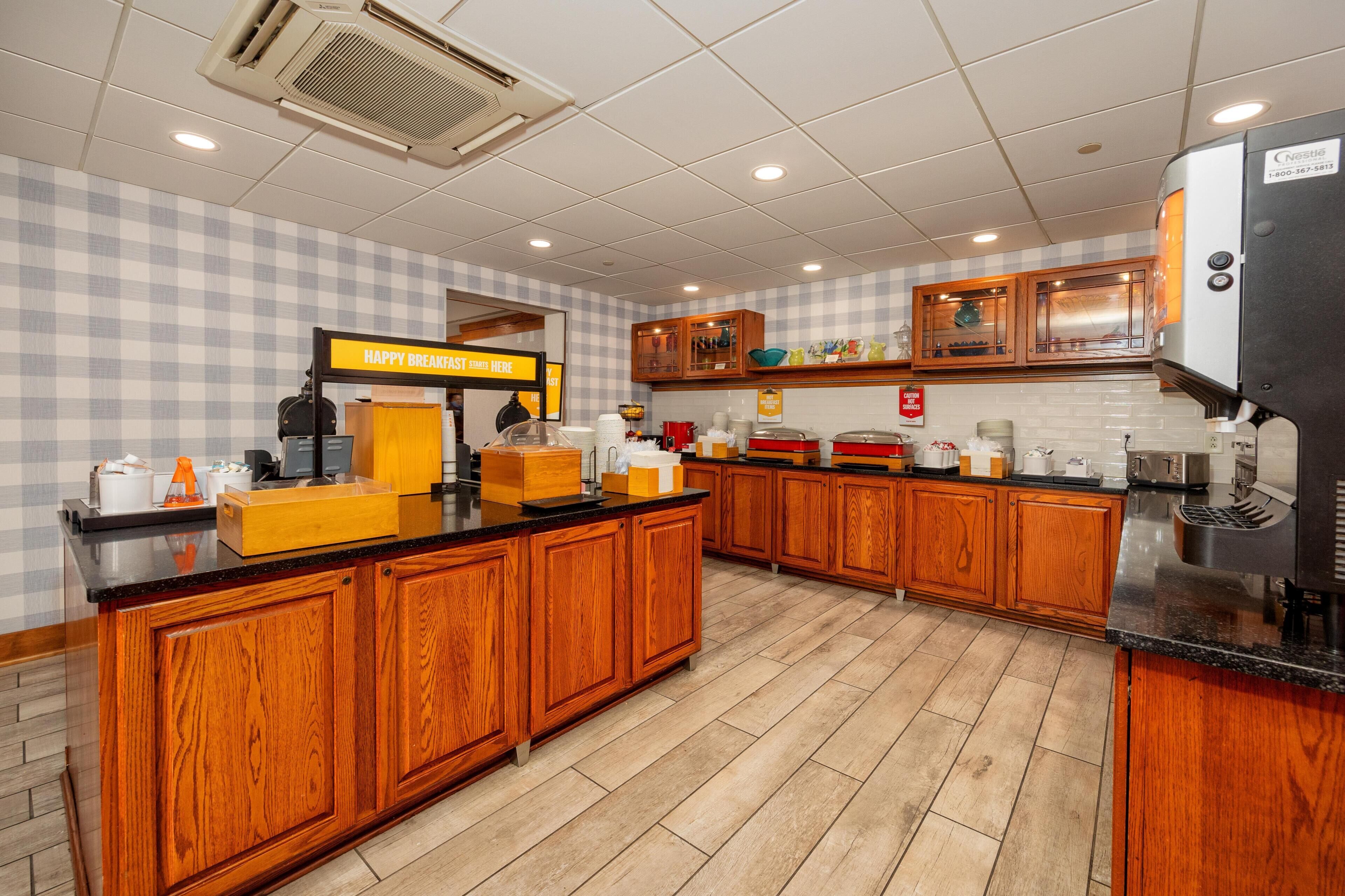 A kitchen with wooden cabinets, a coffee station, and a sign that reads 'HAPPY BREAKFAST HERE.'
