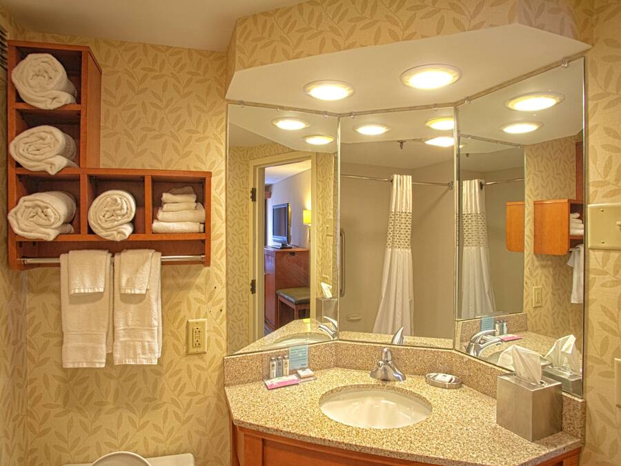 Un baño con lavamanos, espejo, toallero y cortina de ducha.