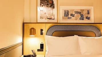 Habitación de hotel con cabecera de madera, mesita de noche con lámpara, teléfono y cuadros en la pared.