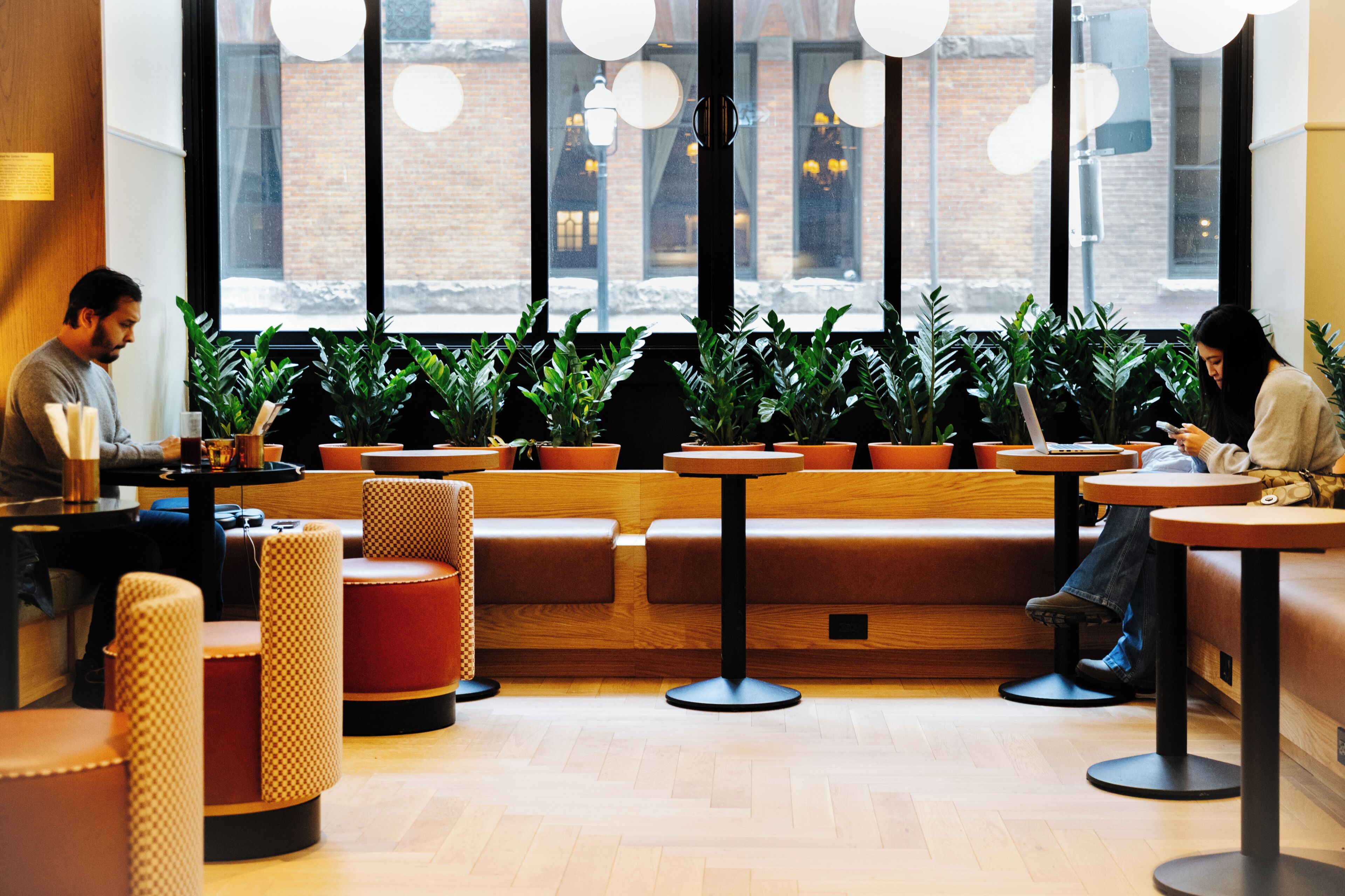 Interior de café com mesas, cadeiras e plantas em vasos.