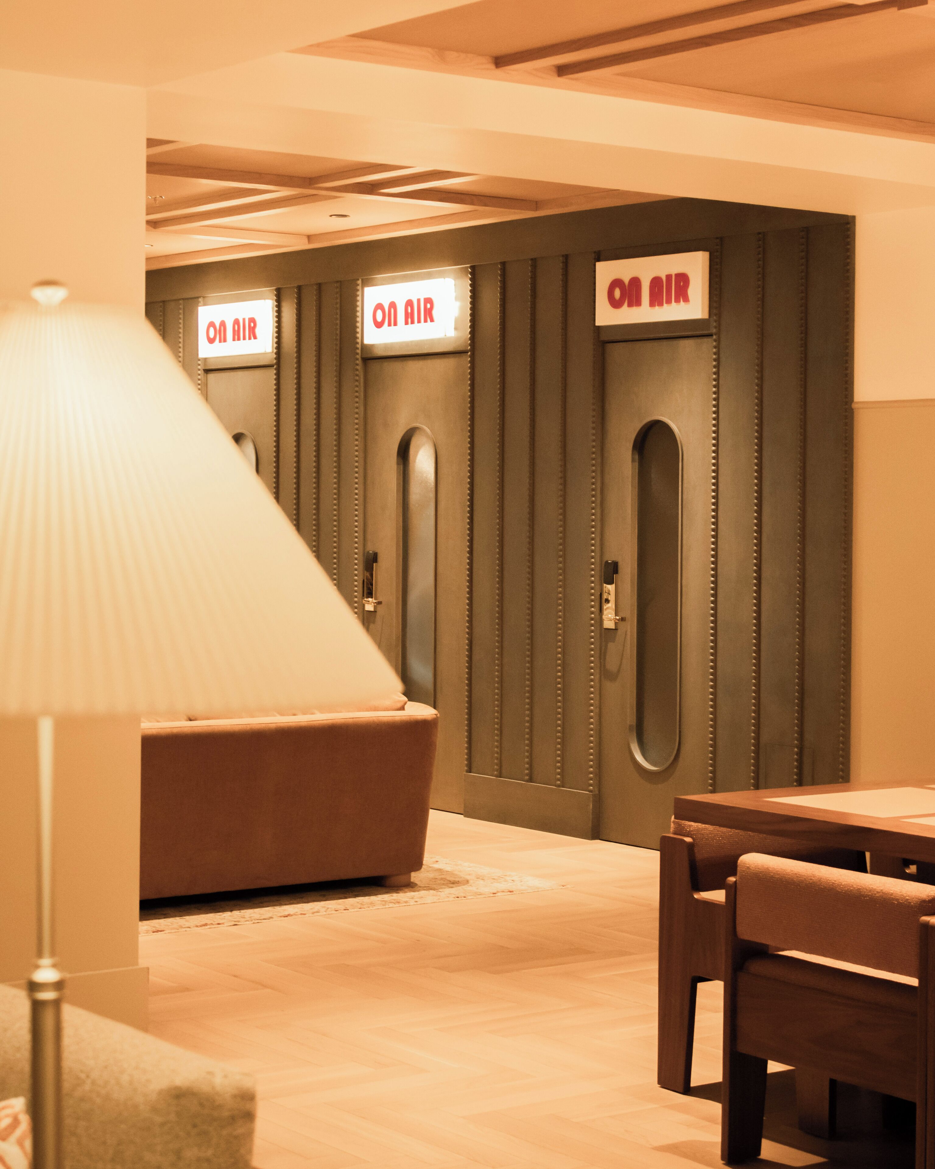 A hotel room with a sofa, a table, and a lamp. There are doors labeled 'ON AIR' and a wall-mounted light fixture.