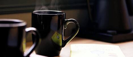 Una taza de café negra, una bolsita de té y un libro sobre una mesa de madera cerca de una ventana.
