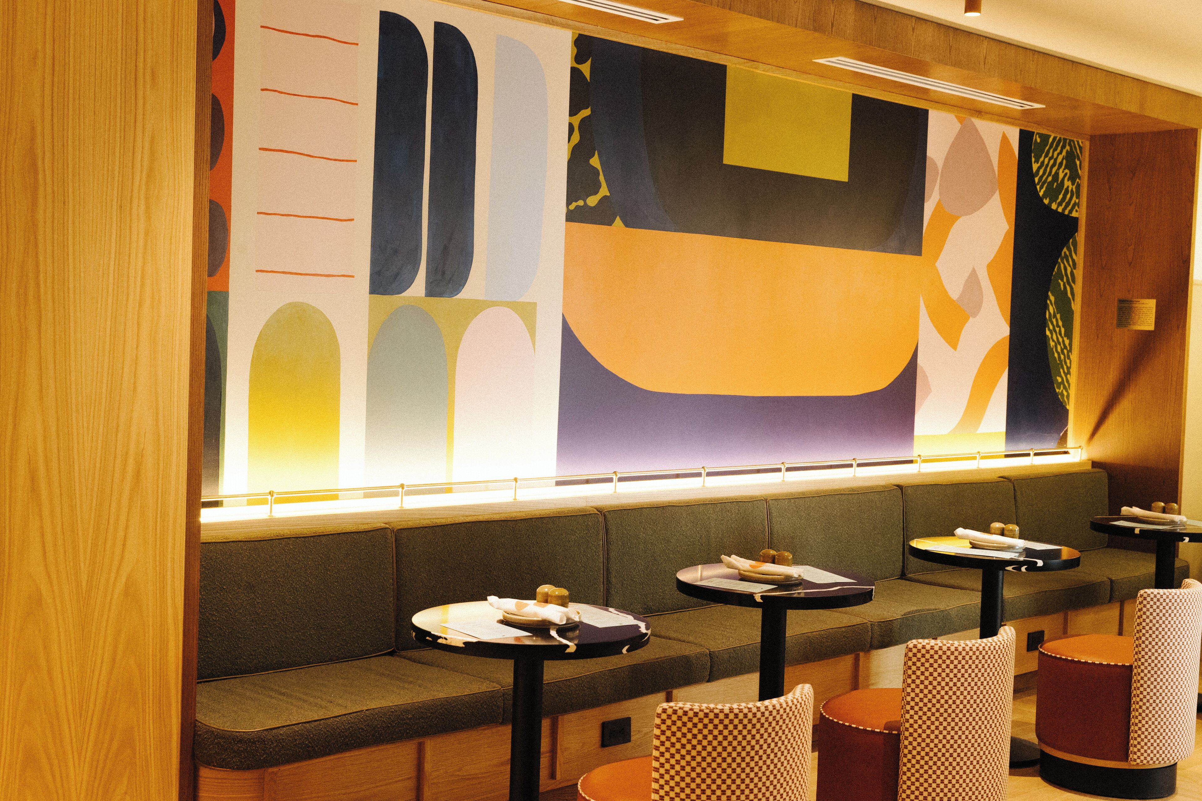A restaurant with a long counter, cushioned seating, and small round tables.