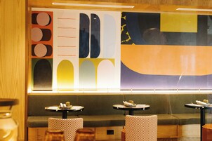 Een restaurant interieur met een grote abstracte muurschildering, zachte zitplaatsen en kleine ronde tafels.