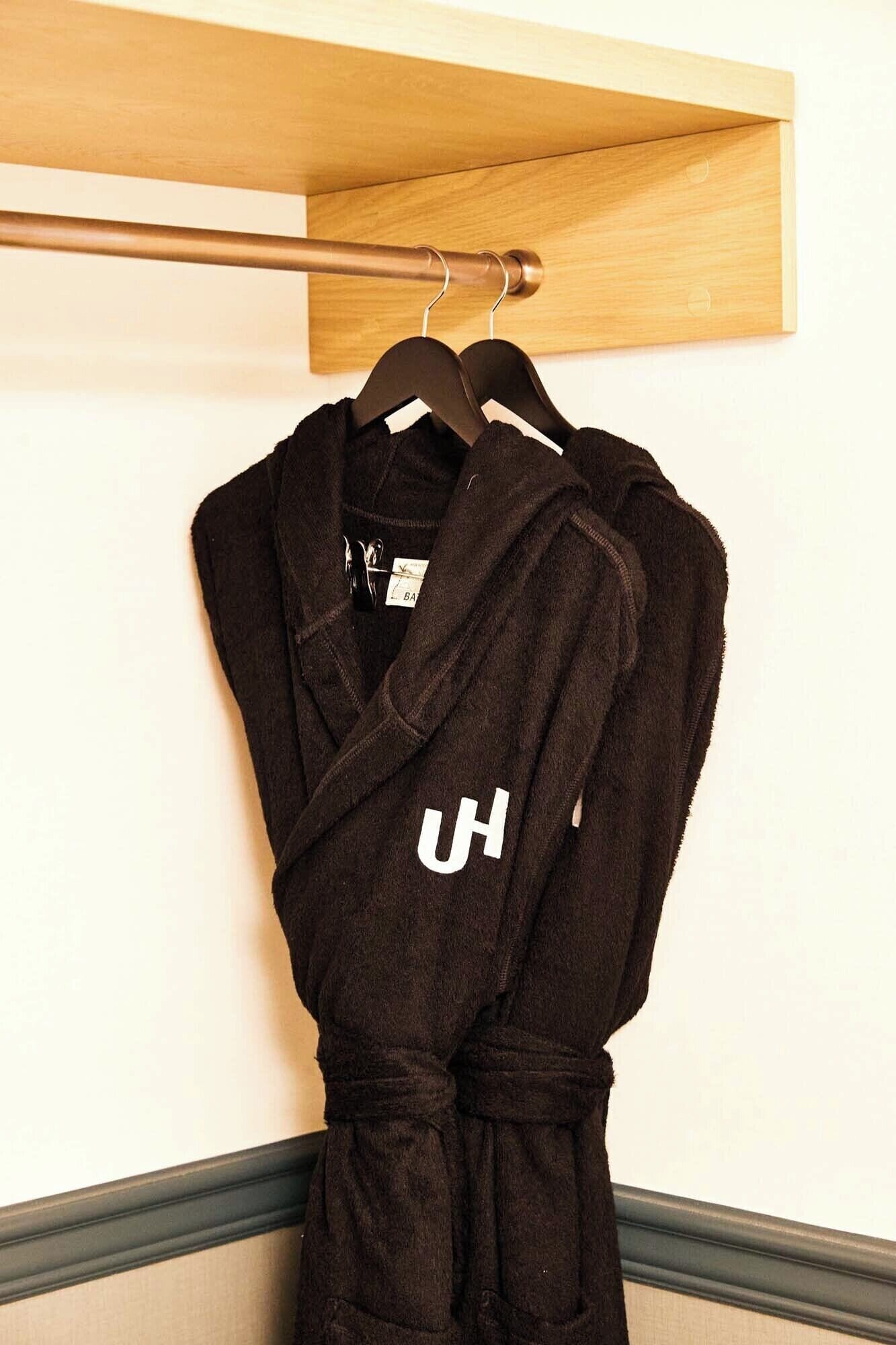 A black robe hanging on a wooden hanger against a wall with a wooden shelf above it.
