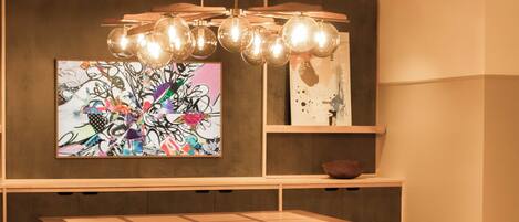A dining area with a wooden table and benches, a modern chandelier, and a colorful abstract painting on the wall.