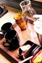 Een dienblad met drie zwarte mokken, een glas amberkleurig vocht en een klein bakje met deksel.