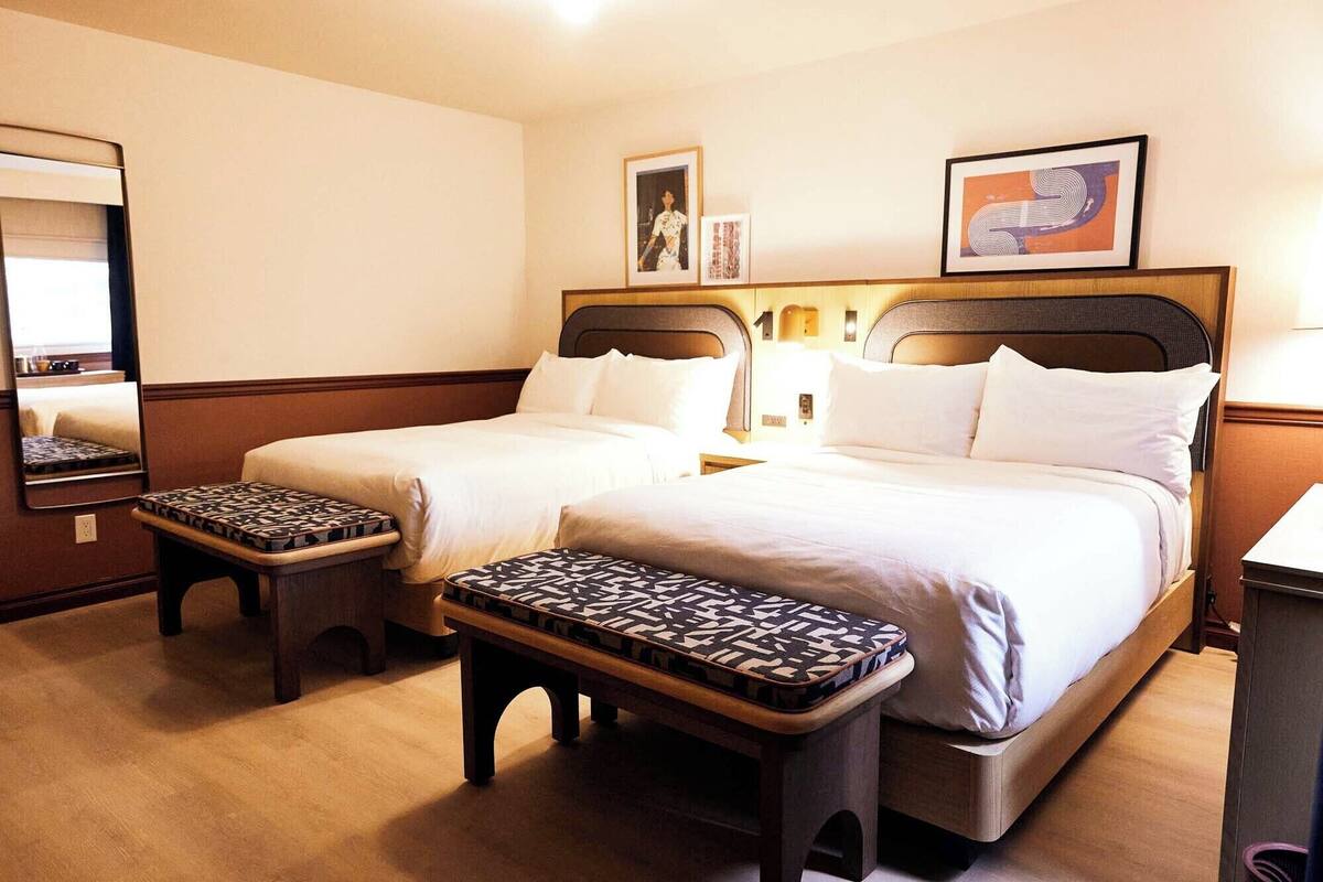 Ein Hotelzimmer mit zwei Betten, einem großen Spiegel und einem kleinen Tisch mit einem gemusterten Kissen.