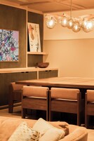 Een moderne eetruimte met een houten tafel en stoelen, een hanglamp en een muur met een kleurrijk abstract schilderij.