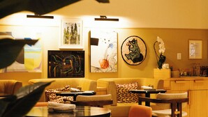 A dining area with orange chairs, a round table, and a sofa. There are wall art pieces and a coffee station. - Union Hotel (Toronto)