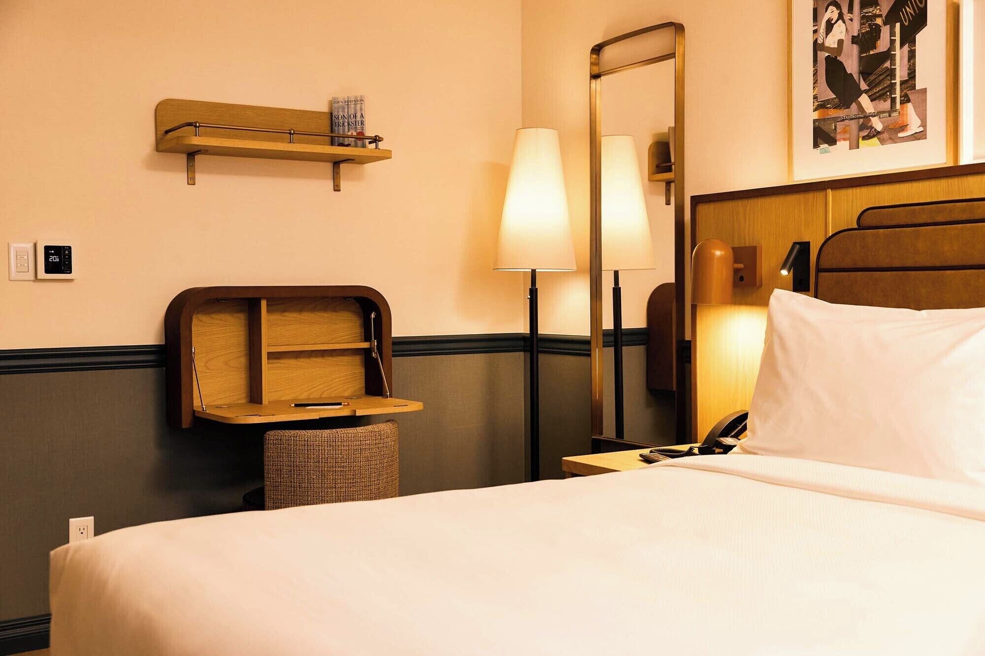 Een hotelkamer met een bed, nachtkastje, lamp, plank en een spiegel.