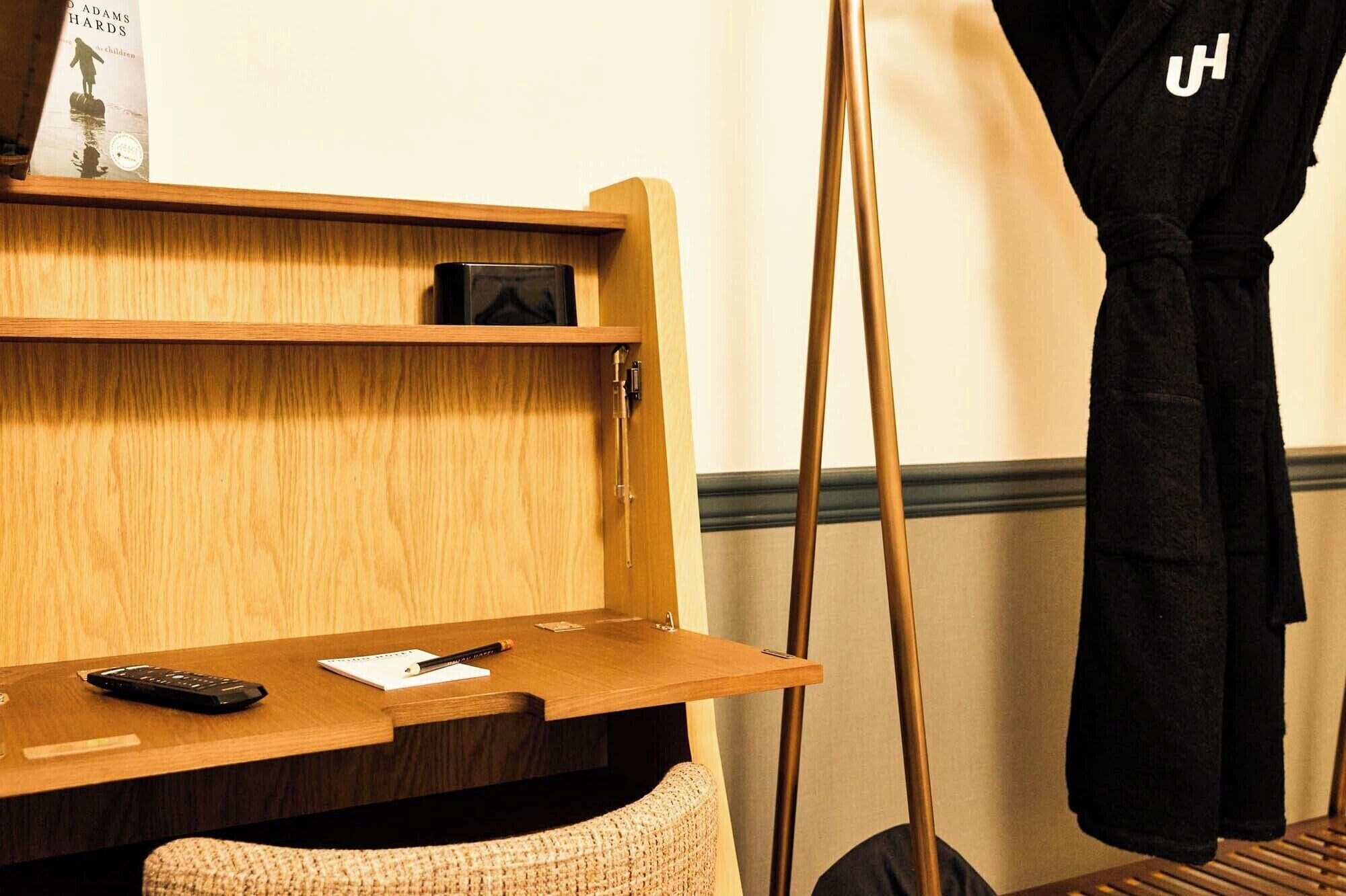 A wooden desk with a remote control, a notepad, and a pen. A black bag hangs on a hook.