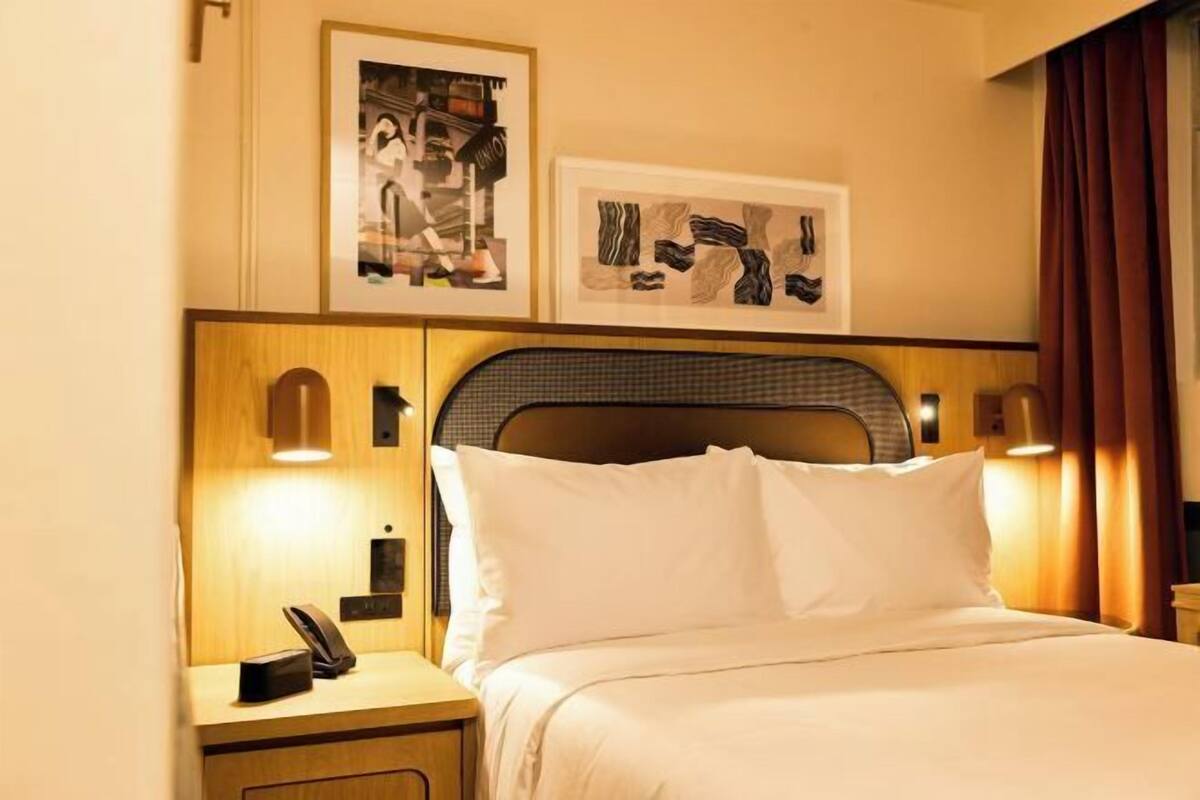 Ein Hotelzimmer mit Bett, Nachttisch, gerahmtem Kunstwerk und Telefon.