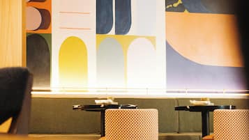 Un interior moderno con un gran mural abstracto, dos mesas y sillas a cuadros.