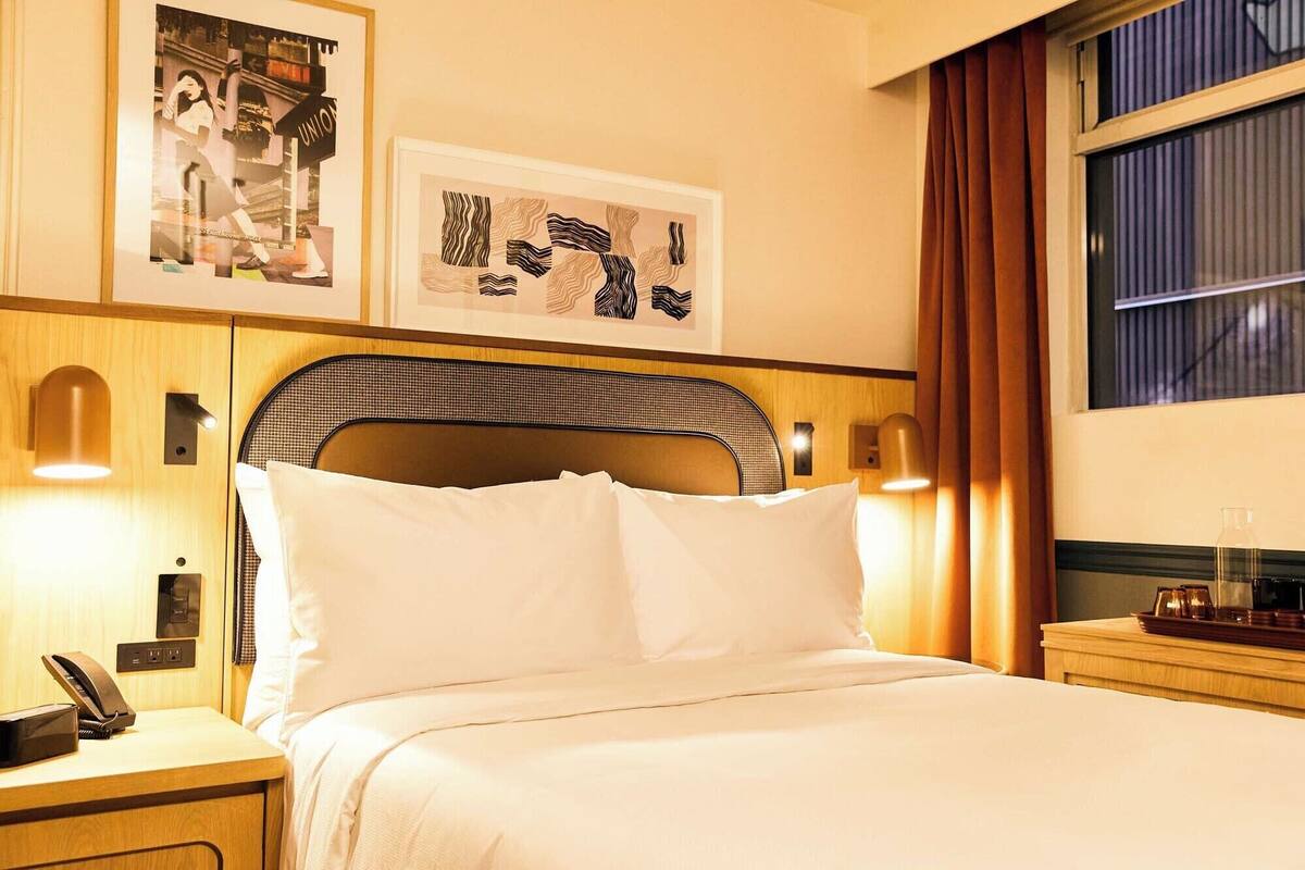 Ein Hotelzimmer mit einem Bett, einem Nachttisch mit Telefon, Wandlampen und gerahmten Bildern.