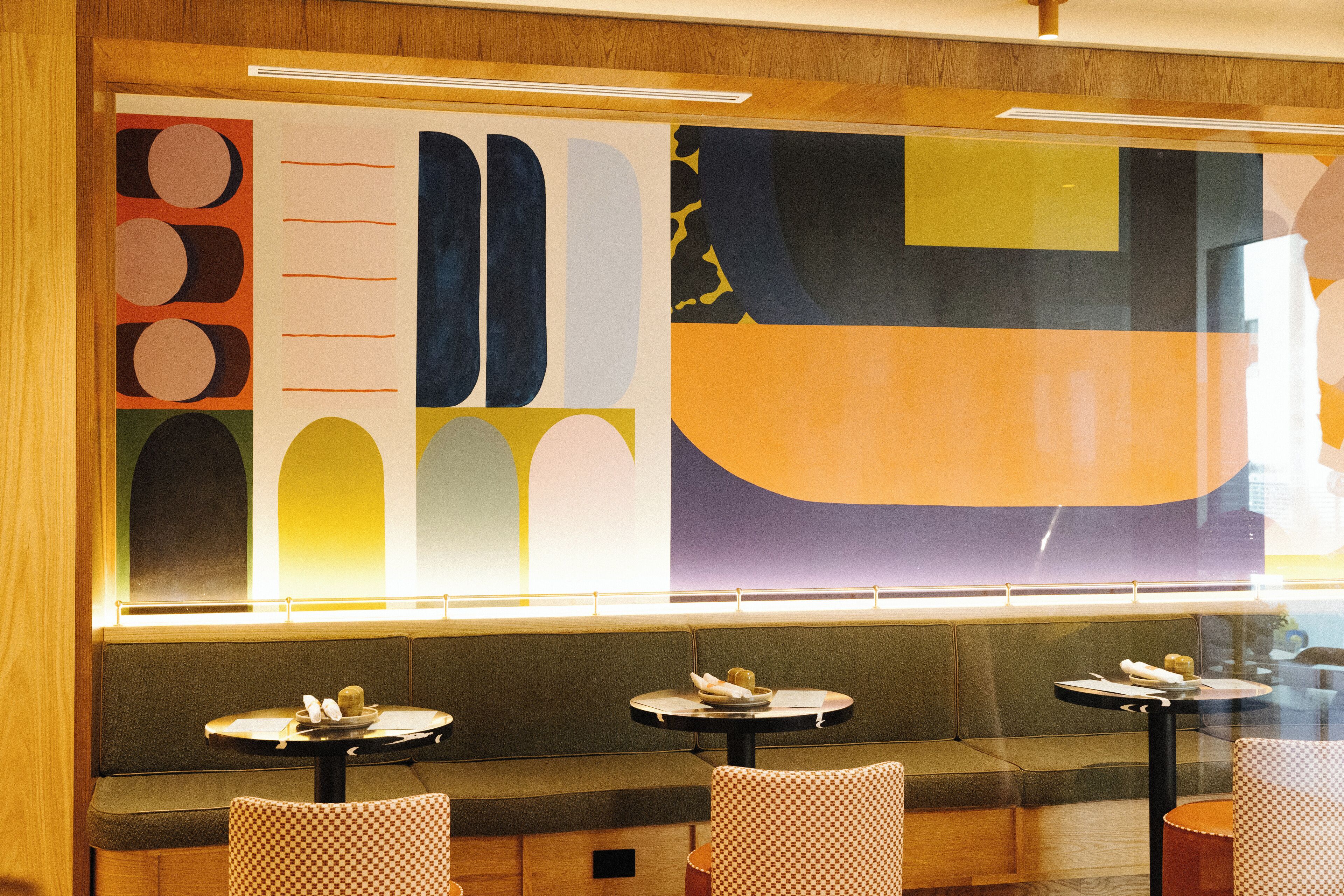 A restaurant interior with a large abstract mural, cushioned seating, and small round tables.