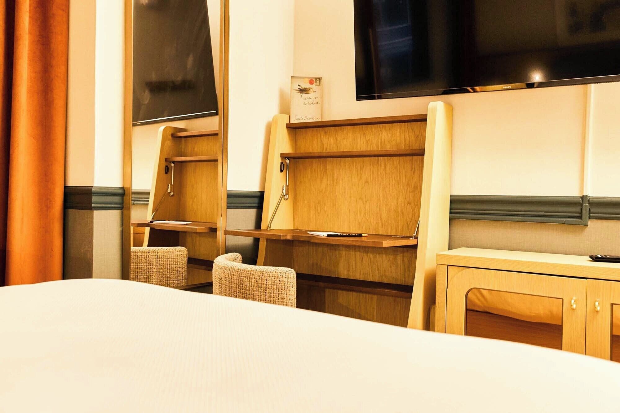 A hotel room with a bed, two wooden shelves, a television, and a small table.