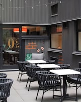 Een terras met tafels en stoelen, een glazen deur en een gevel met verticale lijnen en een raam.