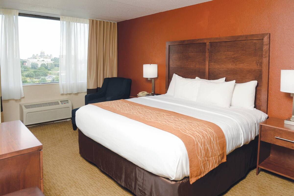 A hotel room with a large bed, a desk, a chair, and a window with curtains.