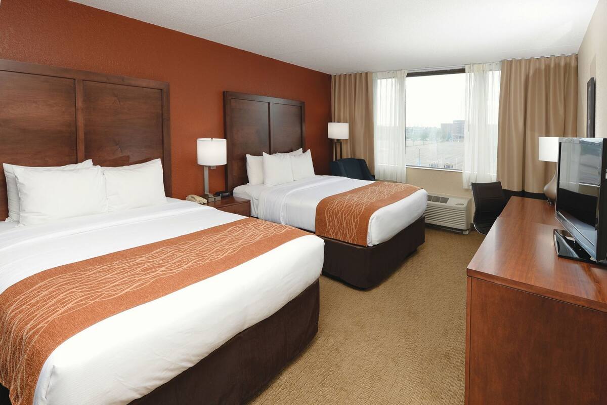 A hotel room with two beds, a desk with a TV, a chair, and a window with curtains.