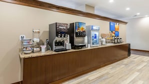 Zona de recepción de hotel con varias máquinas de café, un pequeño espacio de descanso y un mostrador con diversos servicios.