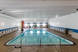An indoor swimming pool with clear water, surrounded by lounge chairs and potted plants.