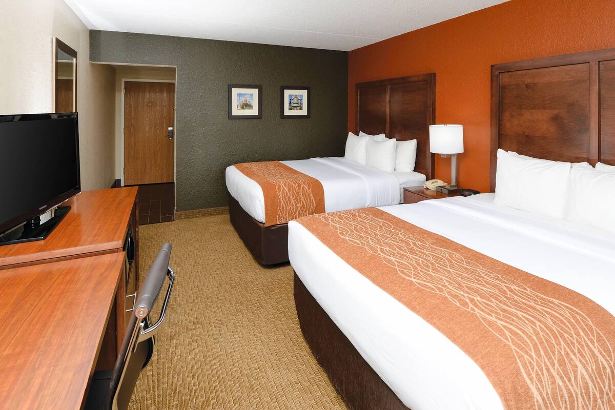 A hotel room with two beds, a desk with a television, a lamp, and framed pictures on the wall.
