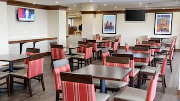 A restaurant with multiple tables and chairs, a television mounted on the wall, and framed pictures on the walls.