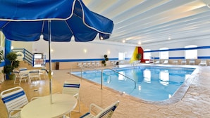 Una piscina interior con decoración azul y blanca, una estación de salvavidas y zonas de estar con sillas y mesas.
