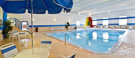Una piscina interior con decoración azul y blanca, una estación de salvavidas y zonas de estar con sillas y mesas.