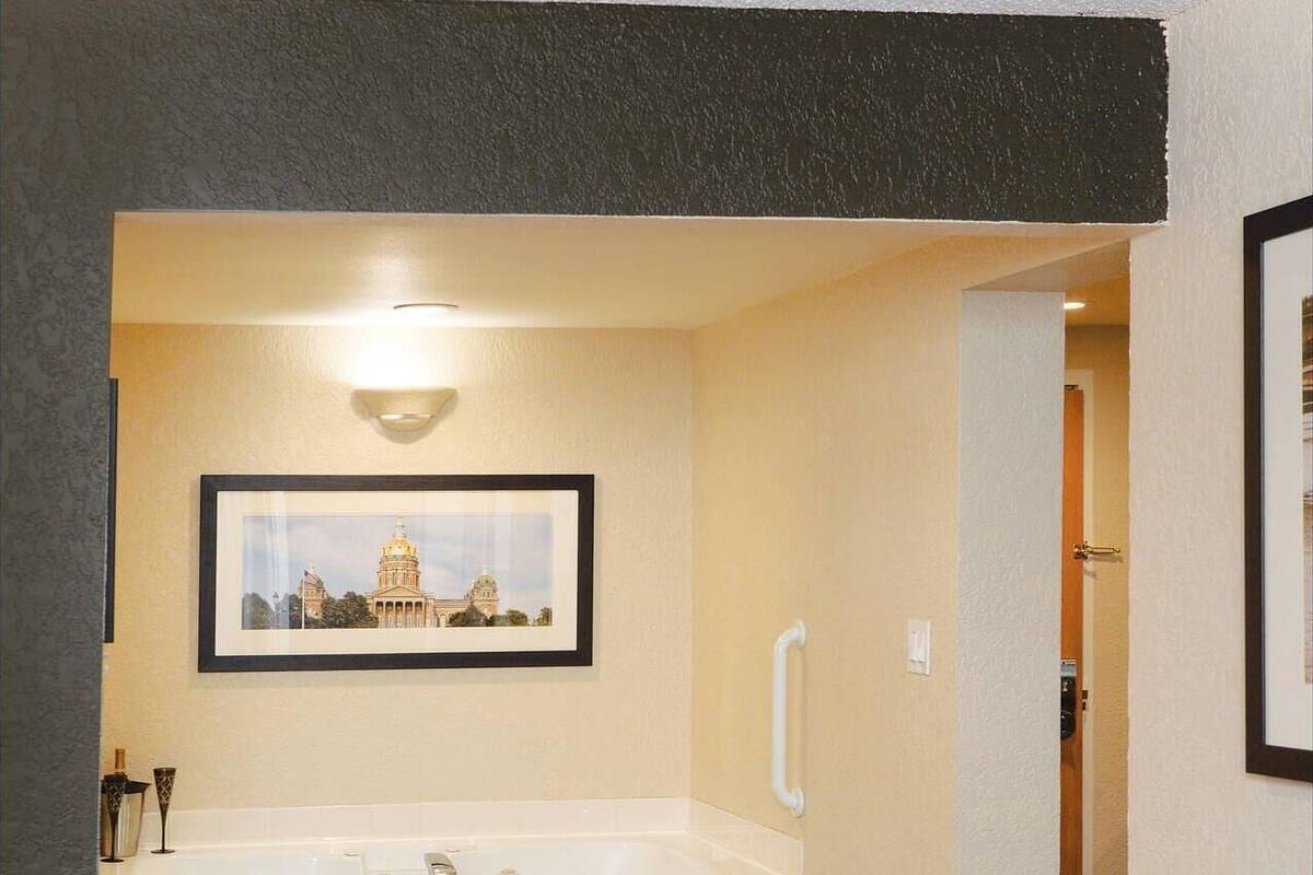 A hotel room with a large bathtub, a framed picture of a building, a bedside table, and a bench.