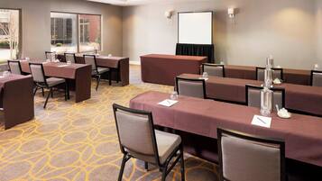 A conference room with multiple tables and chairs, a projector screen, and a carpeted floor.